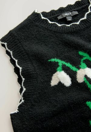 Schwarzes gestricktes ärmelloses Oberteil mit weißen gewellten Kanten und einem weißen Blumenmuster mit grünen Stängeln an Ausschnitt und Armausschnitten.
