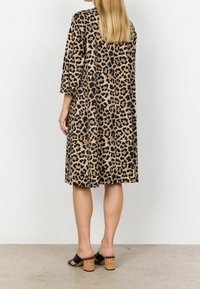 Eläinkuosi, beige mekko mustilla pilkuilla, kolmivartiset hihat, väljä malli, polven pituinen. Päällä mustat korkosandaalit, joissa on korkkikorko.