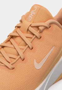 Κοντινή λήψη αθλητικού παπουτσιού Nike σε ροδακινί χρώμα με πλεκτό ύφασμα, κορδόνια, λογότυπο Nike στο πλάι και μαλακή λευκή σόλα.