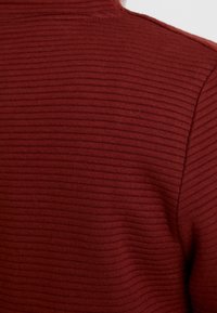 Pull côtelé bordeaux avec une coupe ajustée. Présente un tissu texturé avec de fines lignes horizontales et un col montant.