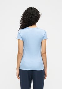 Φωτεινό γ αλάζιο εφαρμοστό μπλουζάκι με κοντά μανίκια, στρογγυλή λαιμόκοψη και λεία υφή. Η πίσω όψη δείχνει στενή εφαρμογή και δομημένη σιλουέτα.