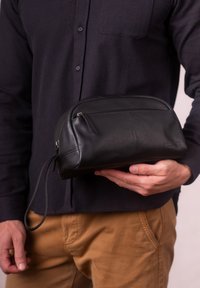 Black leather toiletry bag with a rounded shape, a front zipper pocket, and a hanging loop. Smooth texture and minimalistic design.