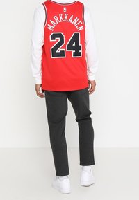 Červený basketbalový dres s bílými rukávy, na kterém je jméno "MARKKANEN" a číslo "24" v černé barvě. V kombinaci s tmavě šedými kalhotami a bílými botami.