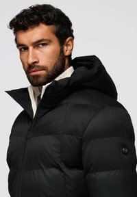 Giacca a vento imbottita nera con cappuccio, caratterizzata da un motivo trapuntato orizzontale e chiusura con zip frontale. Tessuto testurizzato con una finitura elegante.