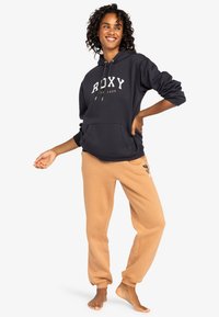 Navy blue hoodie with "ROXY" logo, paired with light tan sweatpants featuring a butterfly design. Soft cotton blend, relaxed fit.