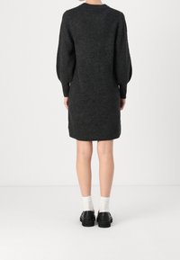 Robe en tricot gris foncé avec manches longues bouffantes, col rond et coupe droite, associée à des chaussures noires et des chaussettes blanches.