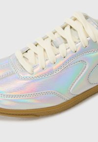 Sneaker iridescente con lacci bianchi, dotato di una superficie liscia e riflettente e di una suola in gomma naturale. Accenti di design curvato sui lati.