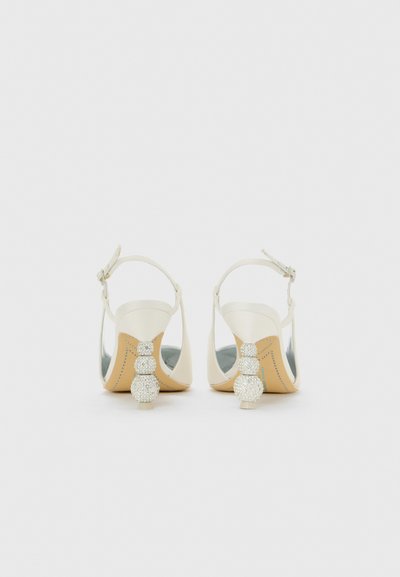 O pereche de tocuri slingback albe cu toc bloc geometric împodobit cu strasuri, văzute din spate pe un fundal alb.