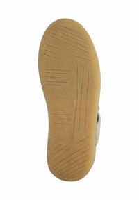 Sole of a slipper with a textured, light brown rubber bottom, featuring grooves and lines for grip. The upper is cream-colored and fluffy.