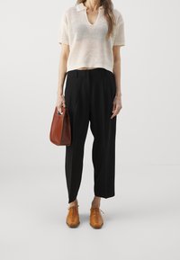 Beige gestricktes Oberteil mit V-Ausschnitt, schwarze gefaltete Hose, braune Handtasche und beige Schnürschuhe. Hat eine lockere Passform und strukturierte Stoff.