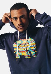 Marineblauwe hoodie met een grote, kleurrijke olifant graphic die geometrische patronen bevat. Inclusief trekkoorden en een voorzak.