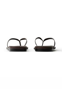 Paar dunkelbraune flache Sandalen mit dünnen Riemen, von vorne vor weißem Hintergrund gezeigt.