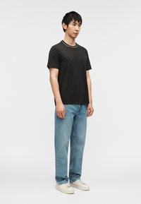 Μαύρο μπλουζάκι με σχέδια, στρογγυλή λαιμόκοψη και λευκή διακόσμηση, συνδυασμένο με ανοιχτό μπλε τζιν παντελόνι με ίσιες γραμμές και κρέμ αθλητικά παπούτσια.