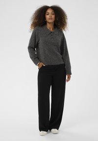 Tamsiai pilka megzta striukė su apykakle ir trimis mygtukais, derinama su laisvomis juodomis kelnėmis ir šviesiais batais.