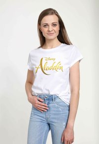 Bílý bavlněný tričko s zlatým nápisem "Disney Aladdin". Krátké rukávy, kulatý výstřih, volný střih. Nosené s světlými modrými džínami s odřením.