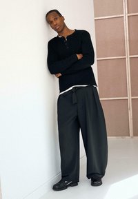 Sort strikket langærmet skjorte kombineret med løse mørke bukser med bindebånd i taljen og sort fodtøj. Minimalistisk design og glat tekstur.