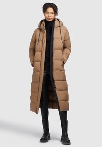 Manteau long matelassé marron avec capuche, poches latérales et fermeture éclair. Présente des sections matelassées verticales et un léger éclat.