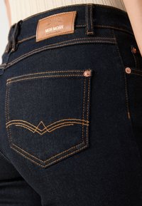 Mörkblå denimjeans med orange sömmar, försedd med en läderetikett vid midjan och detaljerade bakfickor.