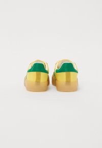 Yellow and green sneakers with a smooth material, padded collar, and a translucent gum sole, featuring a minimalistic design and no patterns.