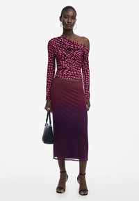 Off-shoulder-Oberteil im pinken und schwarzen karrierten Muster, kombiniert mit einem taillierten, ombre-purpurfarbenen Rock. Schwarze Handtasche und Riemchensandalen.