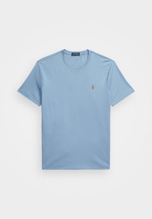 T-shirt en coton bleu clair avec un col rond et des manches courtes, présentant un petit logo brodé sur la poitrine gauche. Texture lisse.