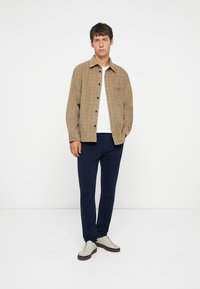 Hnědá kostkovaná košile na knoflíky s jednou náprsní kapsou, v kombinaci s námořnickými slim-fit kalhotami a bílými teniskami. Jednoduchý design a bavlněná textura.