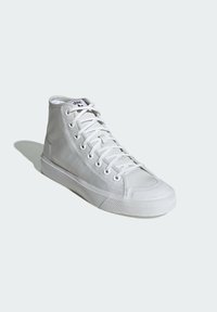 White high-top sneaker with canvas upper, rubber sole, and lace-up design. Features three side stripes and a textured toe cap.