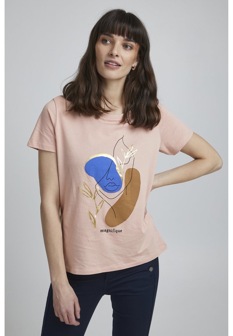 T-shirt en coton rose avec un design graphique aux accents bleus, marron et dorés, représentant un visage et des feuilles, accompagné du texte "magnifique".