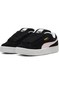 Crne suede tenisice s bijelim gumenim potplatom, s ružičastom Puma prugom i zlatnim logotipom s strane. Tekstura na površini.