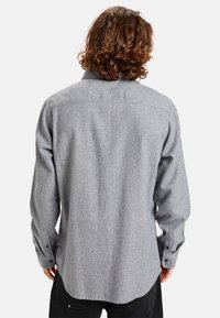 Gray flannel shirt with a button-down collar, long sleeves, and button cuffs. Features a textured fabric and a curved hem.