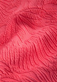 Korallfärgad textil med upphöjda bladmönster och zickzack-sömmar, som visar ett mjukt material med en taktil, tredimensionell effekt.