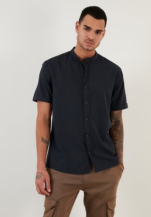 Camisa de botón de manga corta en color azul marino con cuello mao y un ajuste relajado, que presenta una textura suave y un ligero brillo.