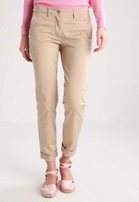 Khaki tapered byxor med en slät textur, som har en knappstängning fram och uppvikt muddar, tillsammans med ljusrosa espadrilloskor.