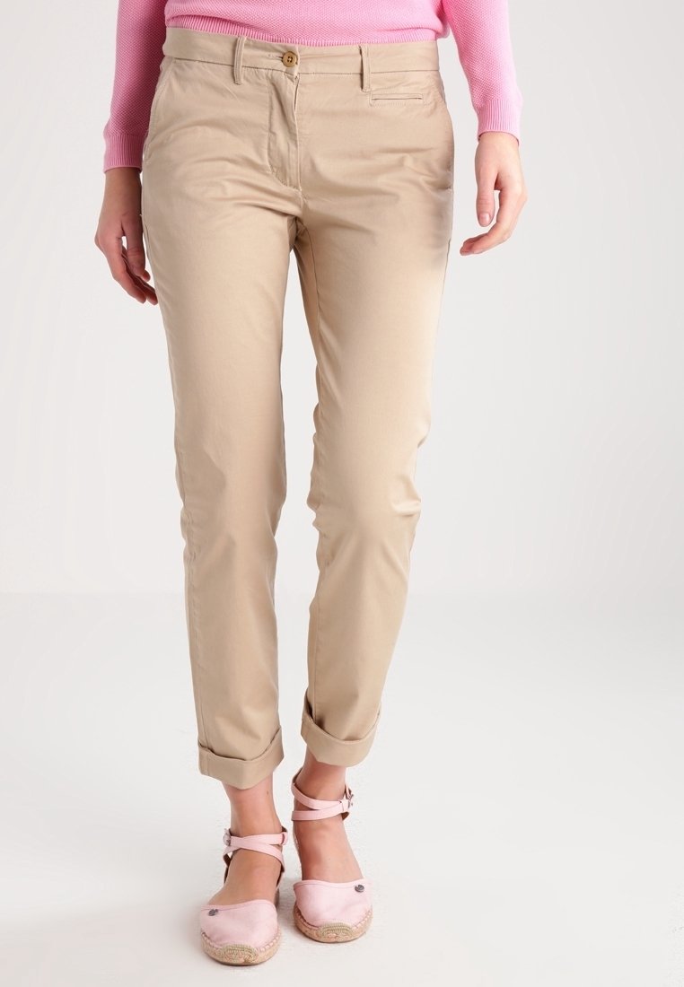 Khaki tapered byxor med en slät textur, som har en knappstängning fram och uppvikt muddar, tillsammans med ljusrosa espadrilloskor.