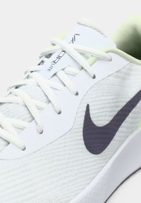 Κοντινό πλάνο άσπρου αθλητικού παπουτσιού Nike με ανοιχτό πράσινο περίγραμμα, άσπρες κορδόνες και μαύρο λογότυπο swoosh σε υφασμάτινο πλέγμα με υφή.