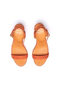 Sandales orange en suède avec une semelle plate, deux sangles réglables et un logo en relief sur la semelle intérieure. Fabriquées en Espagne.