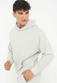 Ljust grå hoodie i mjukt tyg, med dragsko i huvan, framficka och ribbade muddarna för komfort och passform.