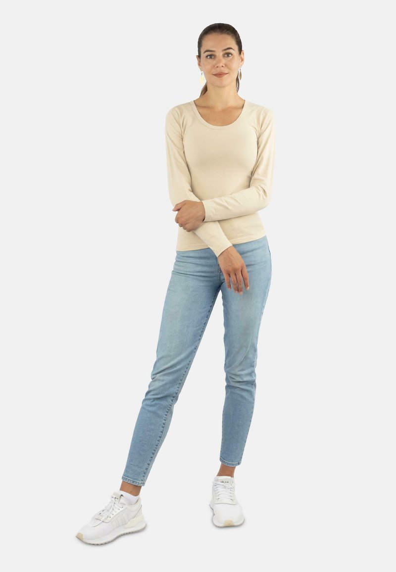 Langärmliges, cremefarbenes Oberteil mit rundem Ausschnitt, kombiniert mit hellblauen Skinny-Jeans und weißen Sneakers. Schlichtes Design, glatte Textur.