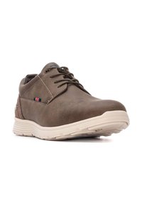 Zapato de cuero marrón con punta redonda, cordones, suela color beige y un pequeño acento azul, blanco y rojo en el lateral.