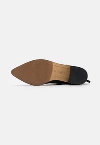 Semelle noire de chaussure en forme pointue, avec une surface en caoutchouc texturé et un talon brun clair. Taille 37 imprimée sur le côté intérieur.