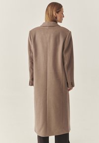 Langer, beiger Mantel aus Wollmischung mit geradem Schnitt, Revers mit Kerbe und geknöpften Manschetten. Glatte Textur, minimalistisches Design.