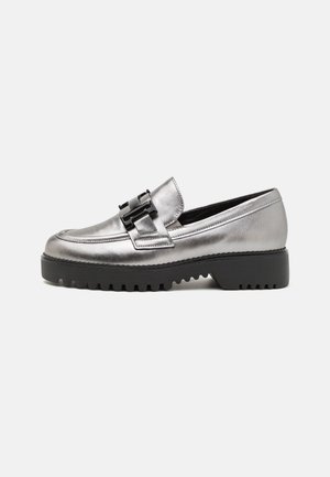 Metalliske sølv loafers med en sort accent spænde, en chunky sort sål, og en glat finish, der har en afrundet tå og syet detaljering.