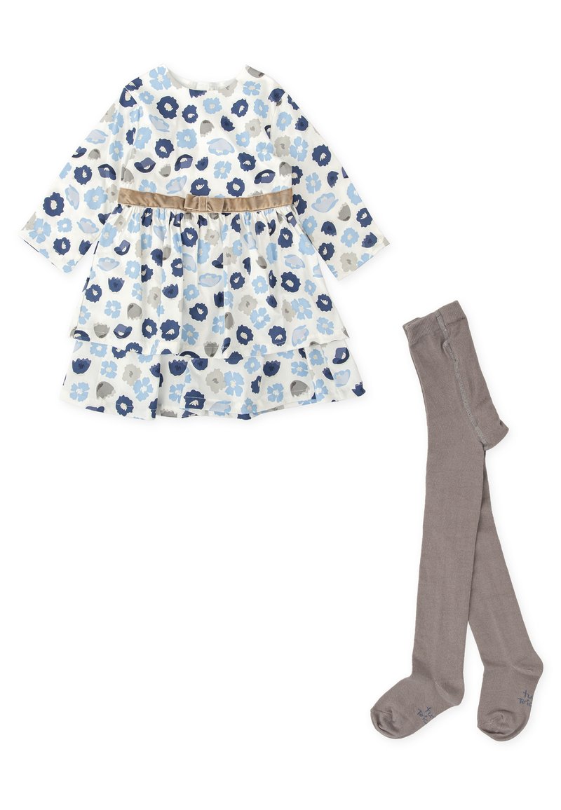 Vestido floral en blanco, azul y gris con mangas largas, una falda de capas y una cinturilla beige; combinado con medias grisáceas.