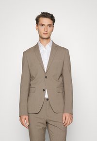 Brown tailored suit made of textured fabric, featuring a single-breasted jacket with two buttons and notch lapels, and matching trousers.