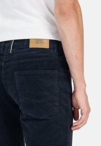 Marineblauwe corduroybroeken met een gestructureerde afwerking, voorzien van een leren label op de tailleband en een achterzak met gebogen stiksel.