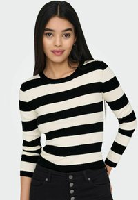 Zwart en crème gestreepte ribgebreide top met een ronde halslijn en lange mouwen, gecombineerd met high-waisted zwarte broek met knoopdetails.