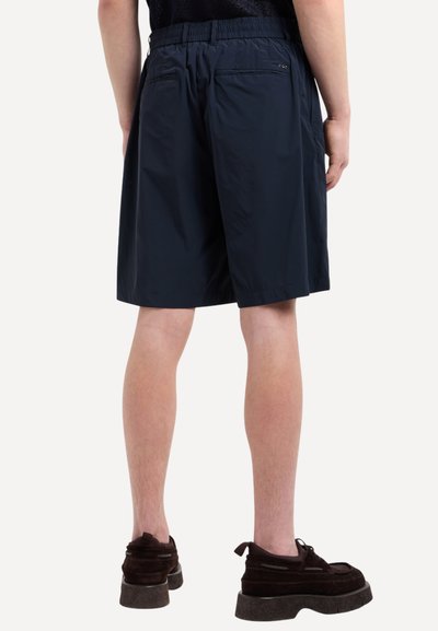 Pantaloni corti leggeri di colore blu navy con vita elastica, dotati di due tasche posteriori e una vestibilità comoda, abbinati a scarpe in suede scure.