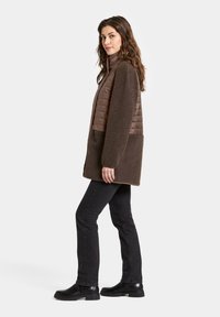 Bruine fleece- en gewatteerde jas met hoge kraag, lange mouwen en zijzakken, gecombineerd met zwarte jeans en enkellaarzen.