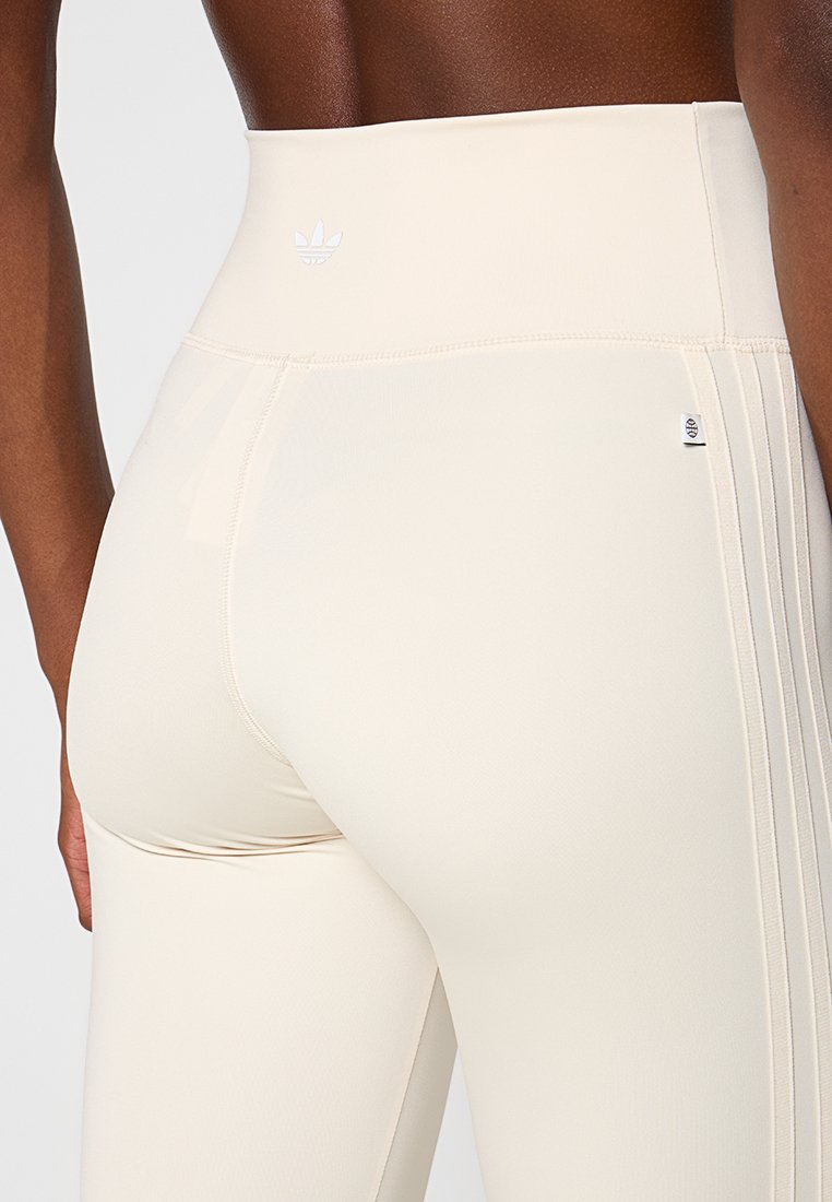 Leggings a vita alta in tessuto beige chiaro con una texture liscia. Presentano un logo bianco e strisce laterali per un tocco di stile.