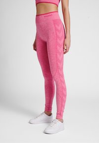 Růžové sportovní legíny s melírovanou texturou, zdobené postranními vzory ve tvaru šipek a vysokým pasem. Kombinovány s bílými teniskami.